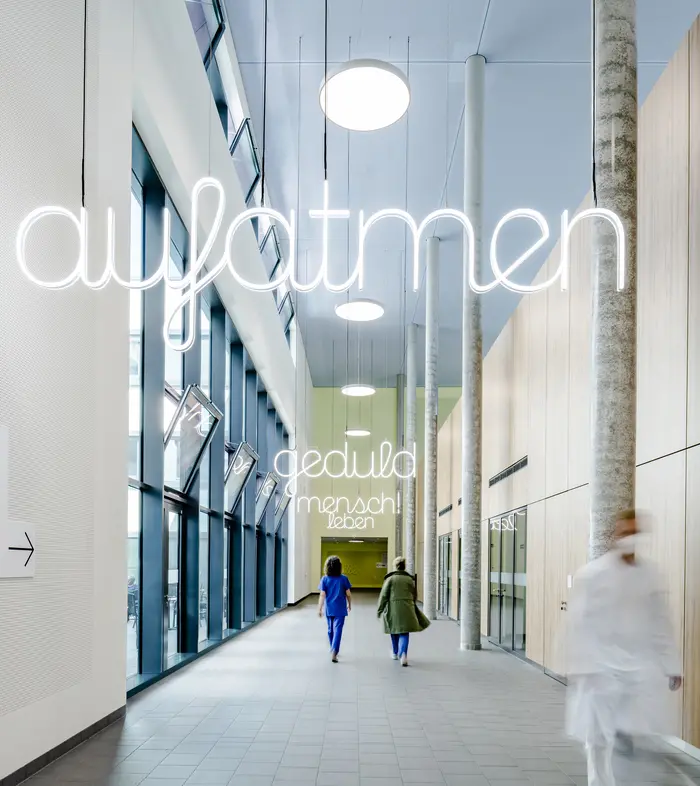 Zwei Frauen laufen einen Gang entlang. Auf Lichtinstallationen steht "aufatmen""
